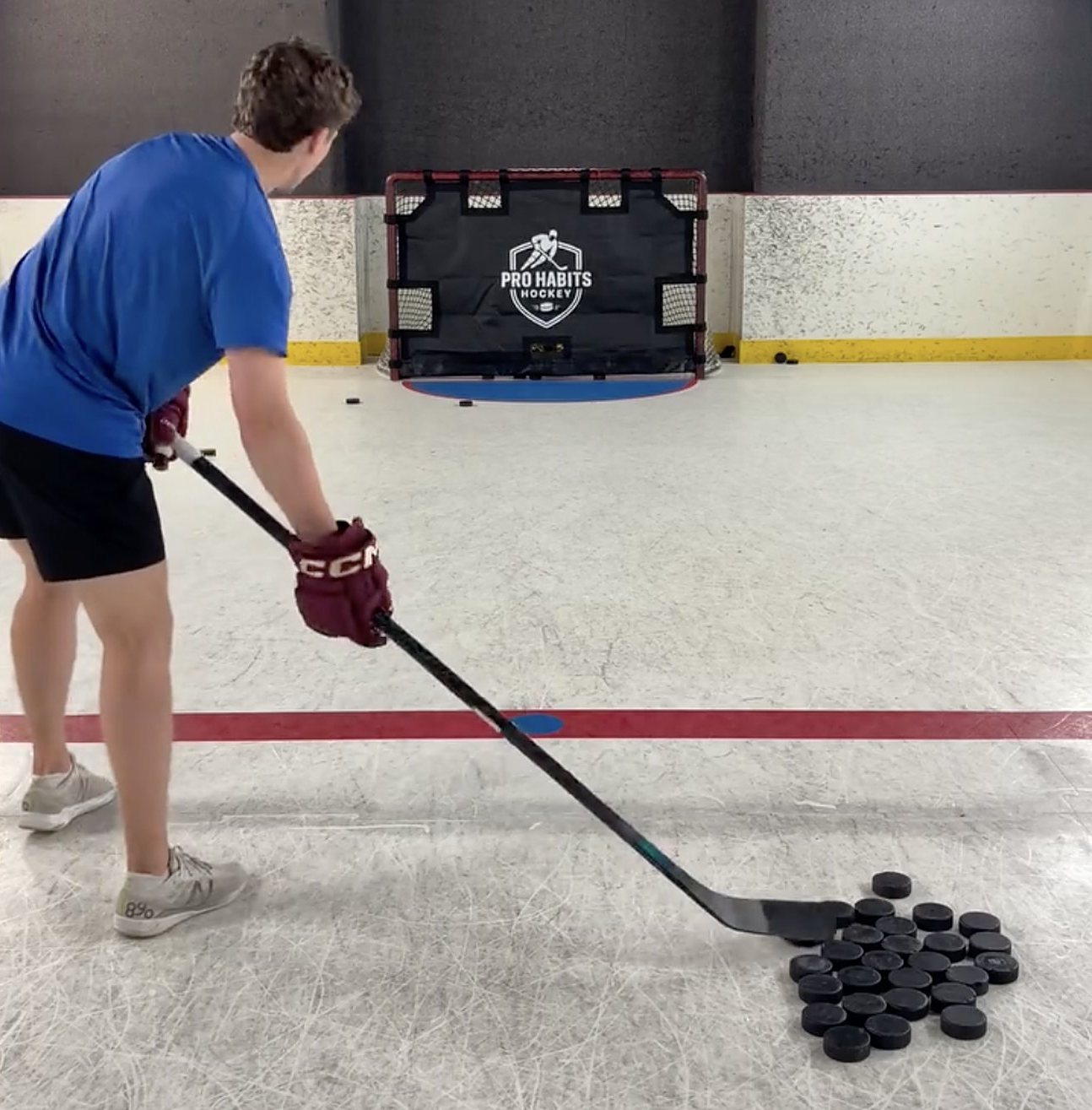 Player taking a shot at a Pro Habits Hockey shooting tarp on the ice, with a pile of pucks